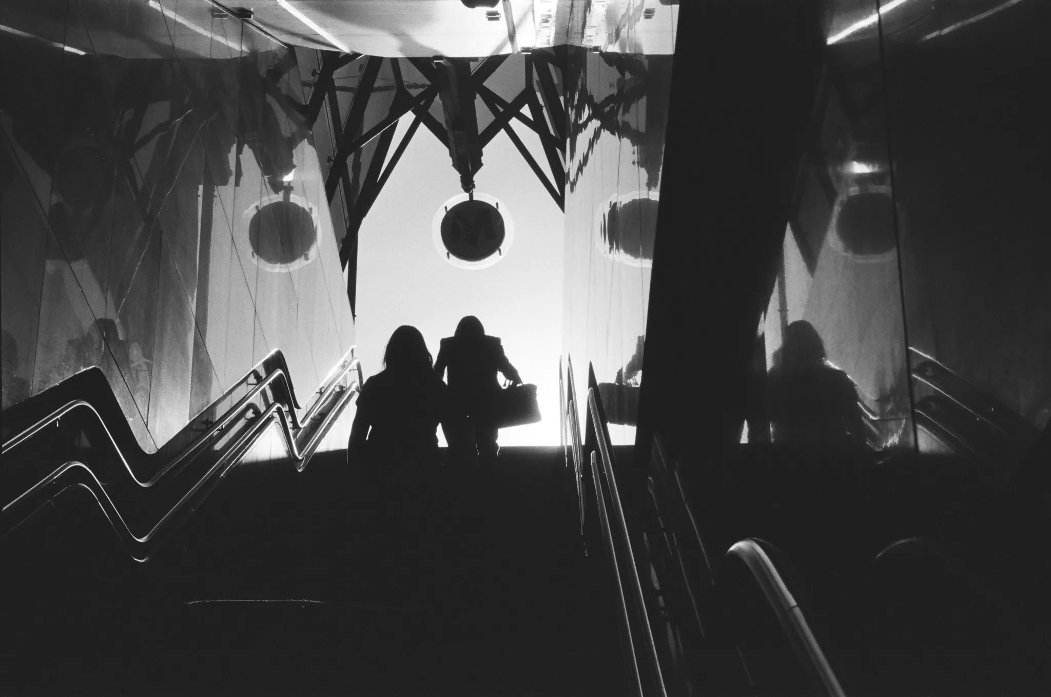 Black and white photo of two silhouetted figures ascending stairs with reflections and geometric shapes.