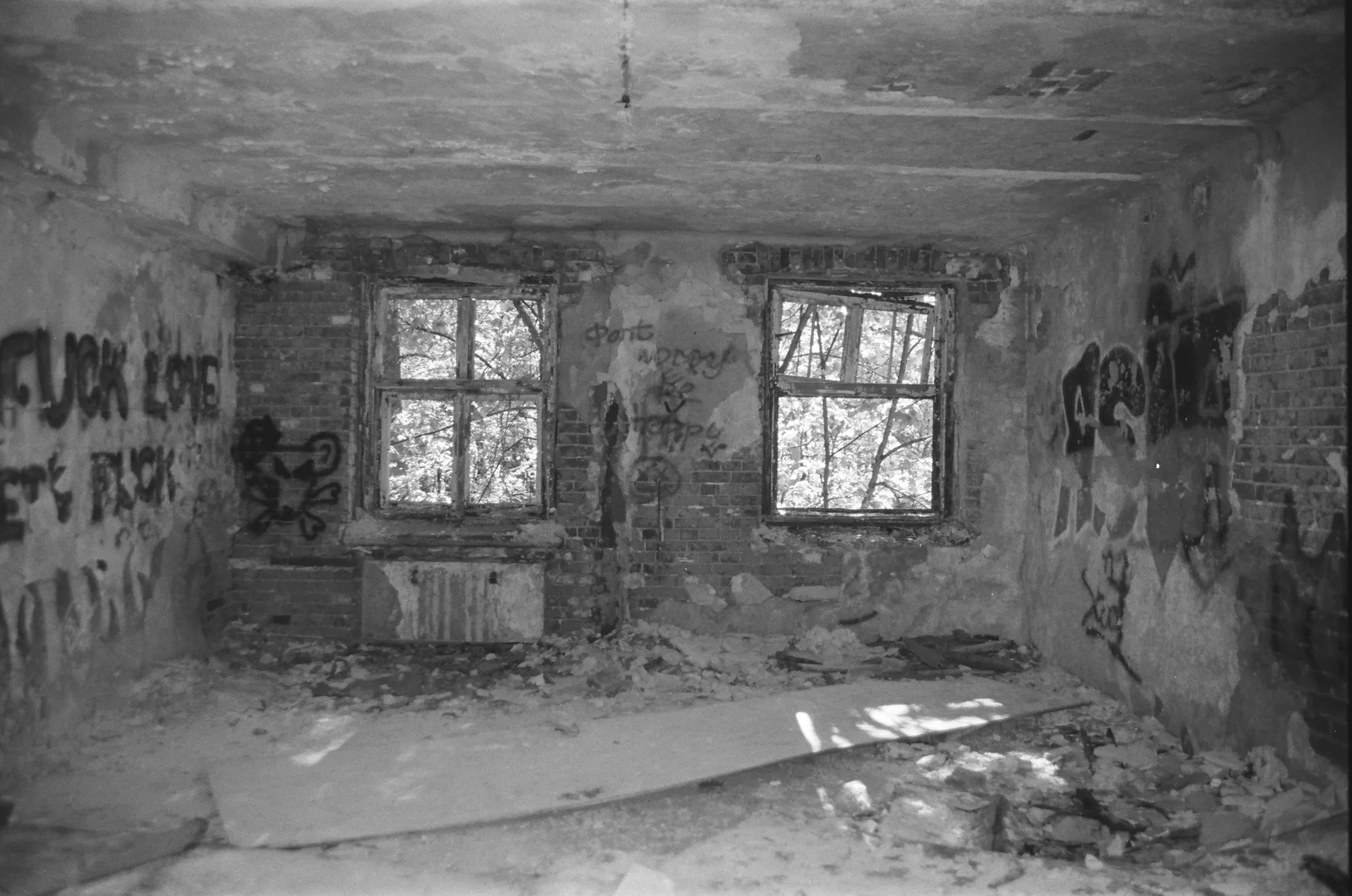 Black and white photo of an abandoned room with broken windows and graffiti-covered walls.