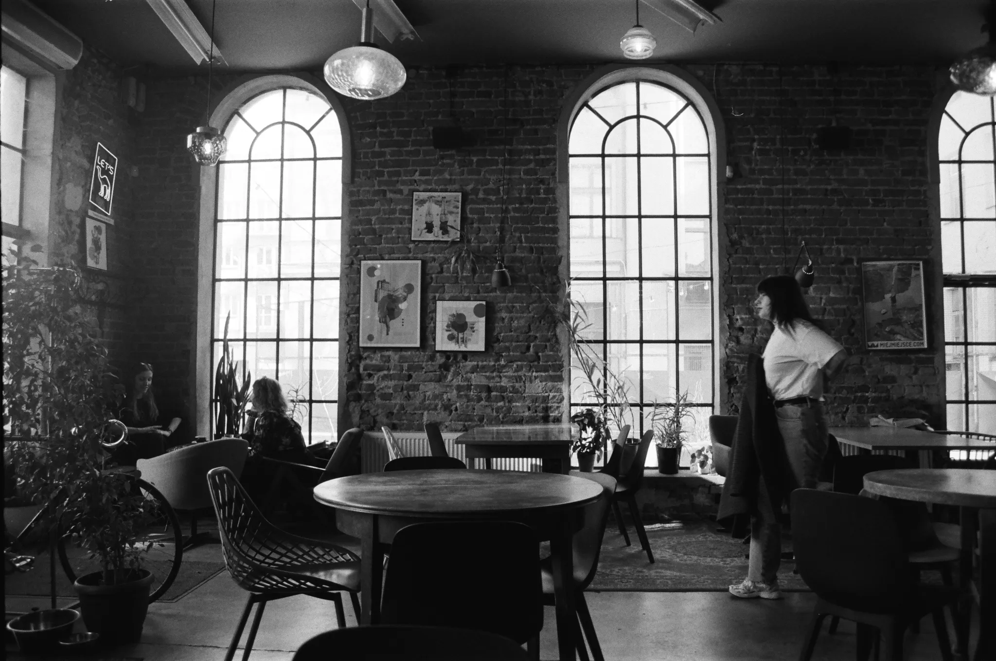Black and white photo of an interior cafe with brick walls and large arched windows.