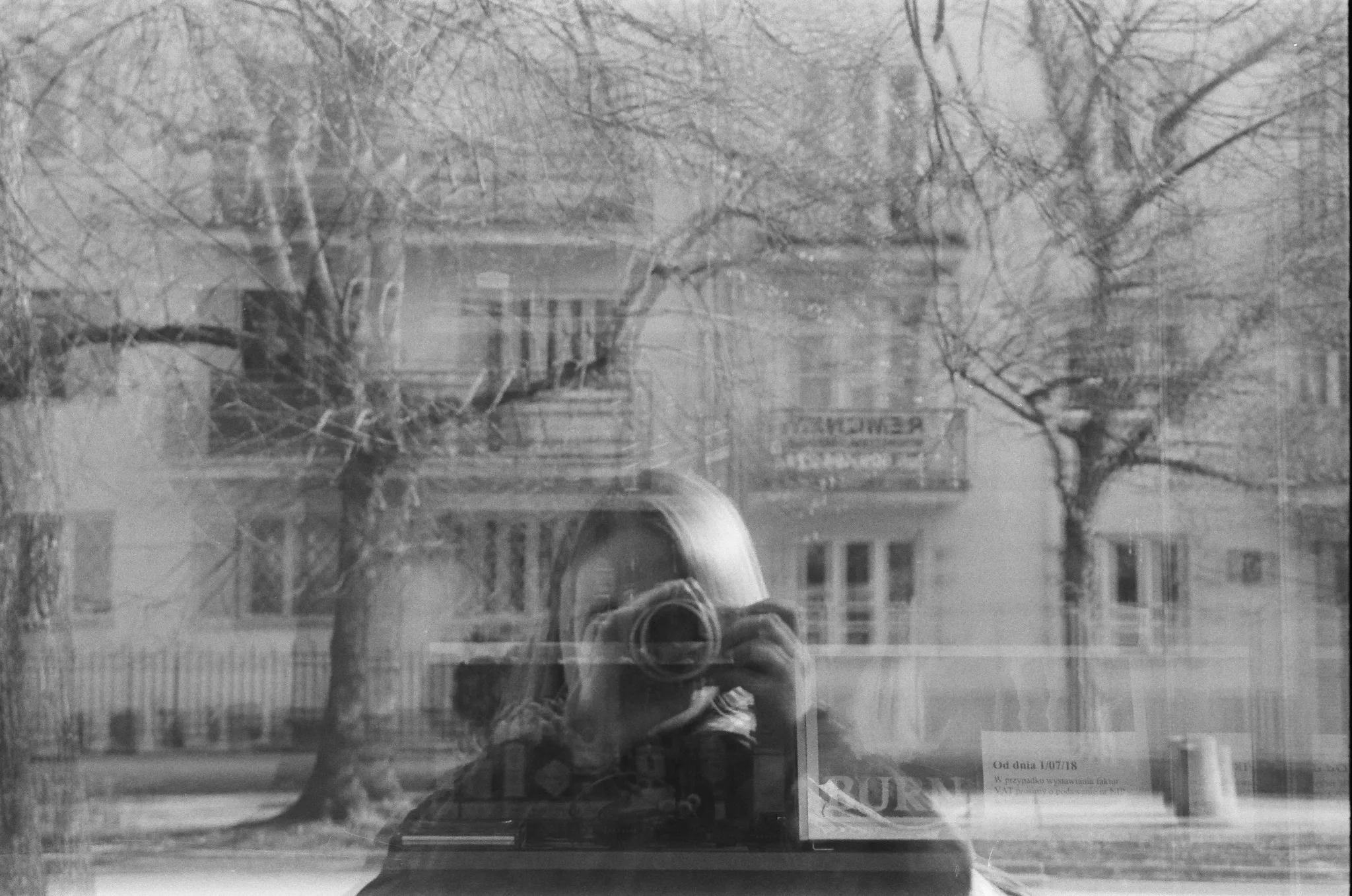Black and white photo of a reflection showing a photographer and trees.