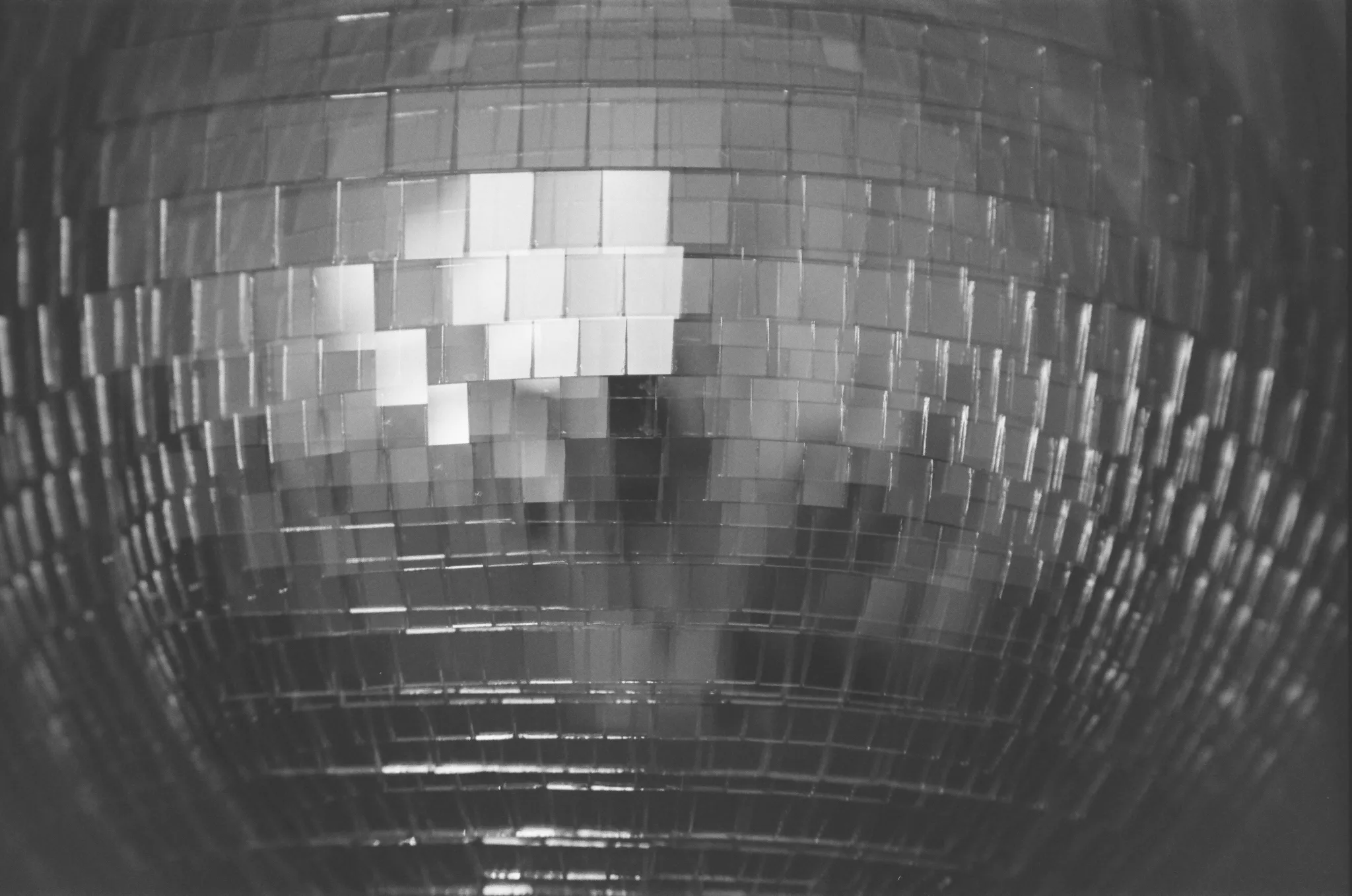 Black and white close-up of a mirrored disco ball reflecting light.