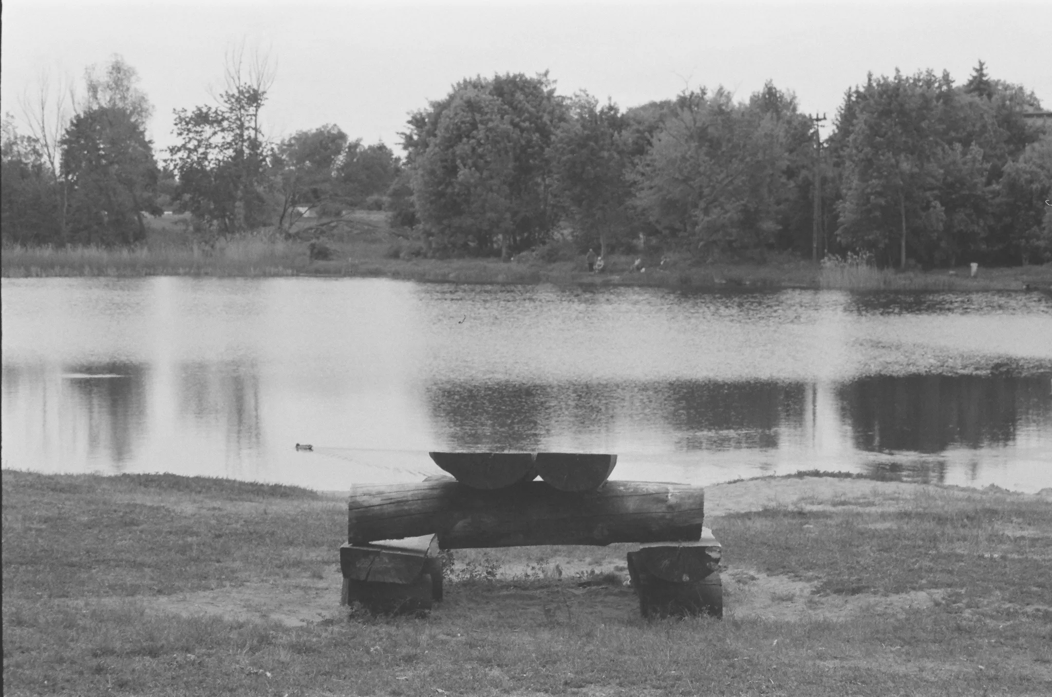 Black and white photo of a serene lake with a wooden bench in the foreground.
